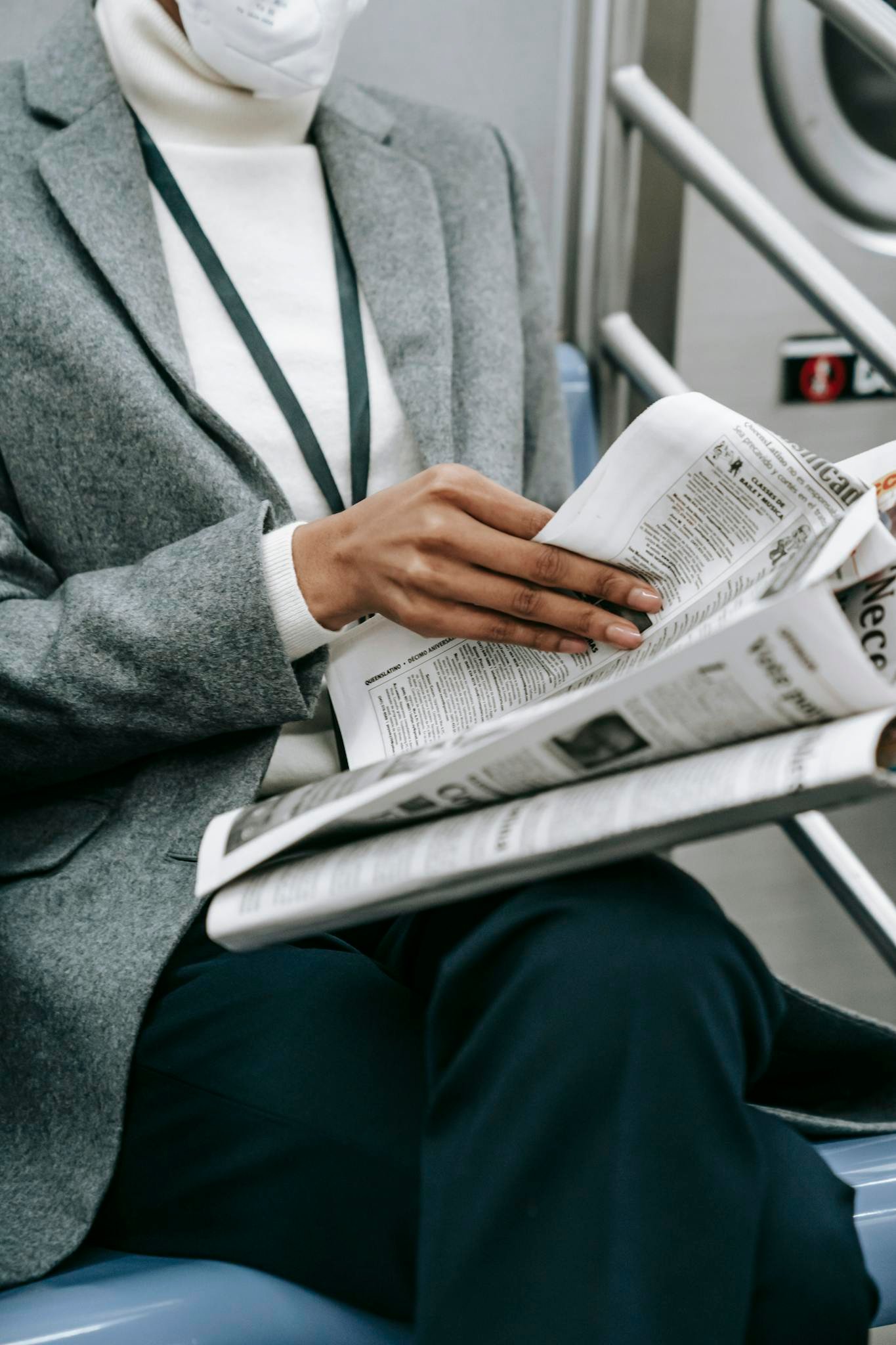 Crop anonymous black female entrepreneur in elegant outfit reading newspaper while riding train